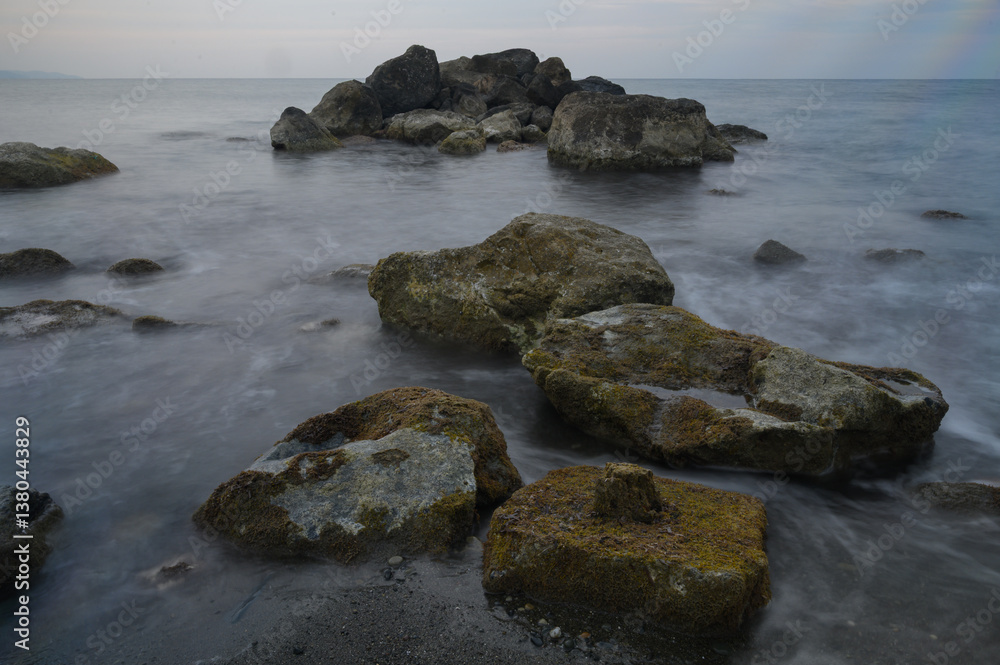 Moss-covered stones emerge from tranquil waters at dusk along the serene coastline Moss-covered stones emerge from tranquil waters at dusk along the serene coastline