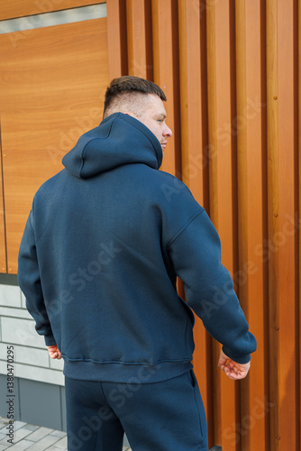Obraz na płótnie A stylish young man wearing a modern and trendy hoodie is confidently posing outdoors, creating a striking visual against a rustic wood panel background that adds character to the scene w salonie