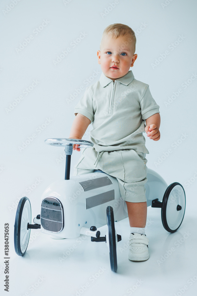 A charming and adorable young toddler is enjoying a delightful moment while sitting in a stylish, vintage rideon toy car, which has been beautifully captured in a bright and cheerful studio setting