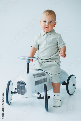Obraz na płótnie A charming and adorable young toddler is enjoying a delightful moment while sitting in a stylish, vintage rideon toy car, which has been beautifully captured in a bright and cheerful studio setting w salonie