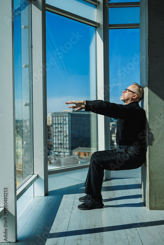 Obraz na płótnie A focused individual meditates by a window, enjoying a captivating city skyline in a serene modern space that enhances mindfulness, promoting reflection, inner peace, and personal growth w salonie