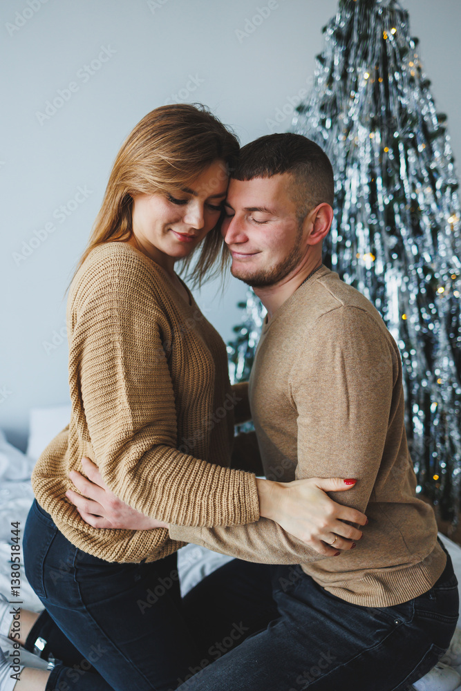 A couple embraces tenderly beneath a decorated Christmas tree, sharing a heartwarming moment of love and joy during the festive season, surrounded by bright decorations and the warmth of winter