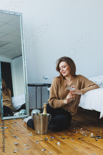 Obraz na płótnie In a stylish bedroom, a young woman enjoys a cozy celebration with champagne, embracing the festive atmosphere with joy, creating lasting memories while relaxing in this charming indoor space w salonie