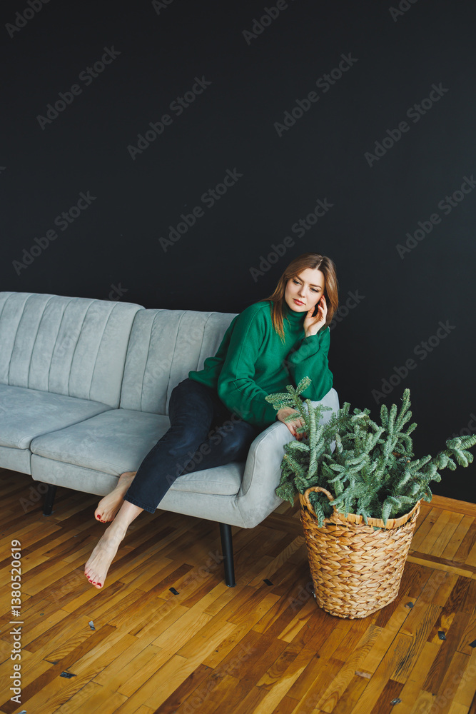 In a beautifully designed living room, a young woman relaxes on a stylish couch, lost in thought, surrounded by vibrant indoor plants that create a soothing atmosphere for tranquility