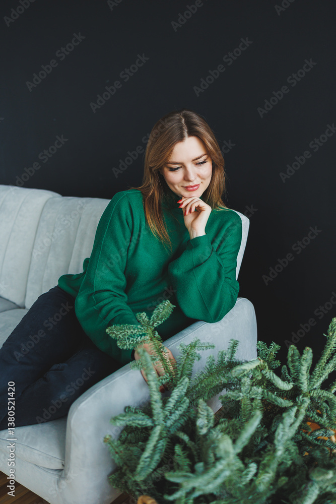 A young woman is comfortably relaxing on a soft couch surrounded by a variety of lush indoor plants, all while wearing a cozy green sweater, which evokes a strong sense of peace and deep tranquility
