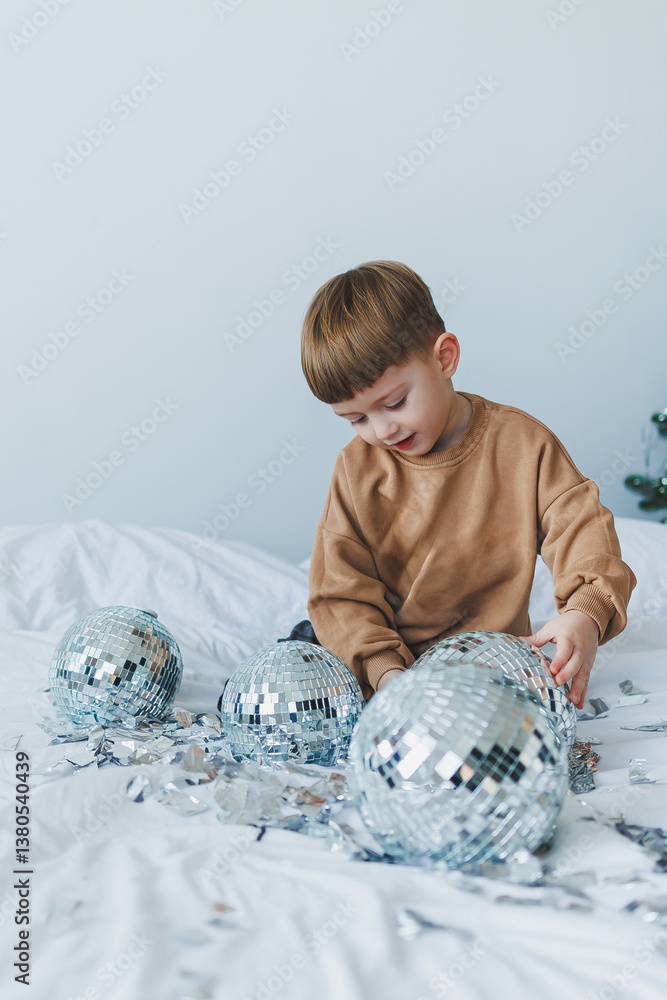 A Joyful Child Engaged in Play with Sparkling and Shiny Disco Balls on a Cozy Bed Nestled Amidst Festive Bedding and Cushions During the Holiday Season Filled with Cheer and Laughter