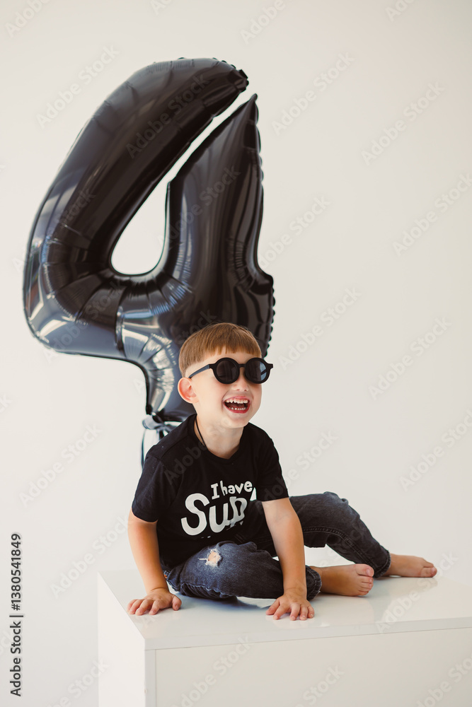 An adorable child joyfully celebrating their 4th birthday party with a fun black balloon in hand and wearing trendy sunglasses, creating delightful memories filled with laughter and happiness