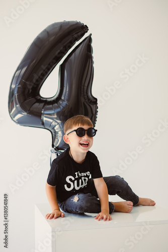 Obraz na płótnie An adorable child joyfully celebrating their 4th birthday party with a fun black balloon in hand and wearing trendy sunglasses, creating delightful memories filled with laughter and happiness w salonie