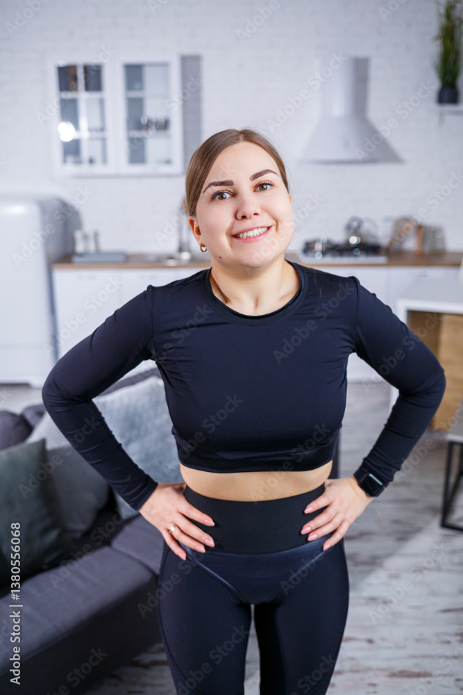 A fit young woman is in a modern home environment, she is smiling broadly and appears ready and enthusiastic to start her workout routine, showcasing both style and physical fitness in her activewear