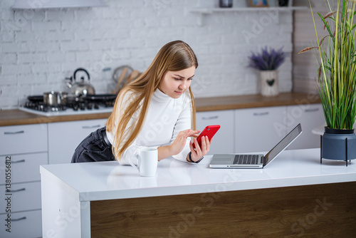 Obraz na płótnie In a modern kitchen, a woman uses her smartphone in a tranquil space with minimalist decor and greenery, creating an ideal environment for multitasking and relaxation during her morning routine w salonie