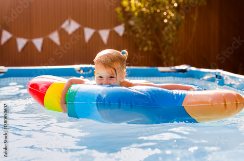 Smiling kid having fun in pool on colorful inflatable toy at summer day