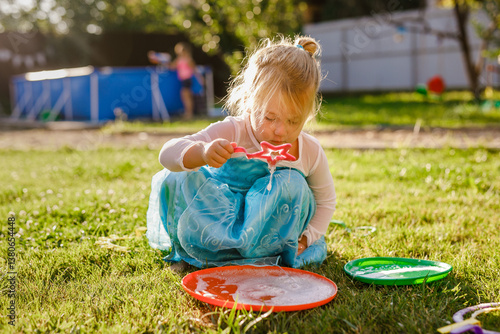Little girl in princess dress blowing soap bubbles in a sunny garden during outdoor playtime