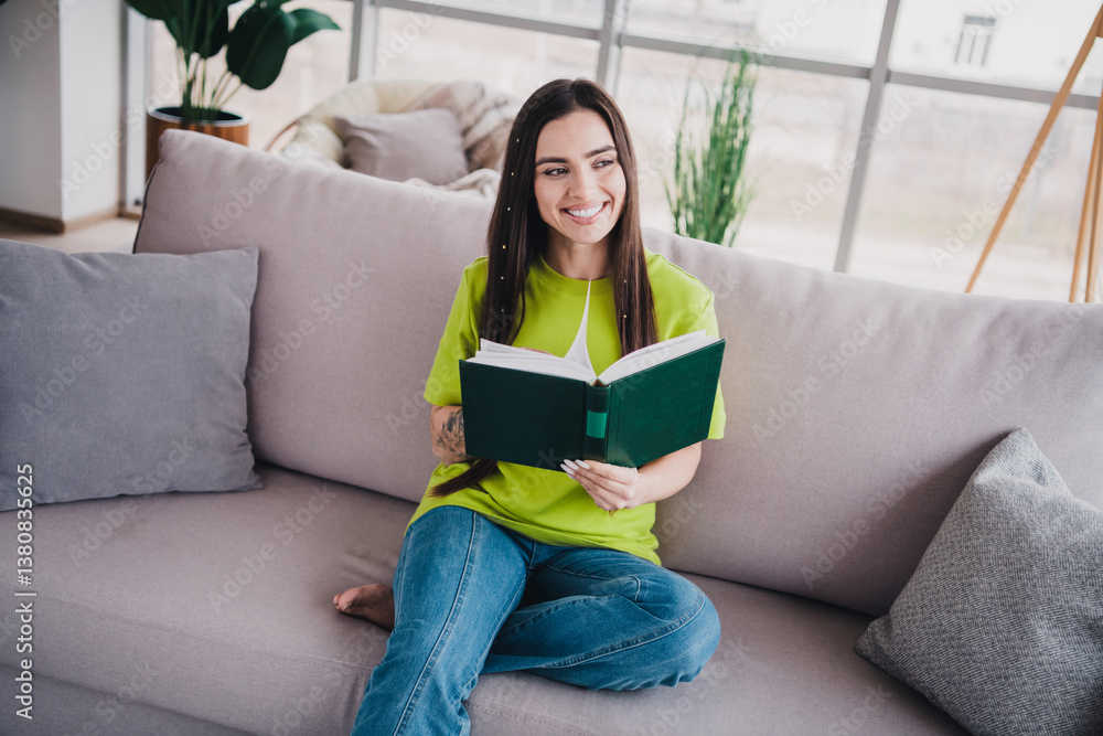 Smiling young woman reading a book on a comfortable sofa in a bright and cozy living room during the day Smiling young woman reading a book on a comfortable sofa in a bright and cozy living room during the day