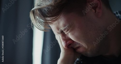 Close up a sad man with blue eyes cries and covers his face with his hand