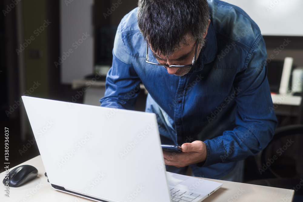 A professional man working with his laptop and smartphone. Business man with glasses focused on his work. Business concept from home. A professional man working with his laptop and smartphone. Business man with glasses focused on his work. Business concept from home.