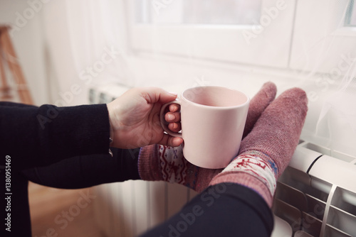 Obraz na płótnie Woman drinking hot tea with her feet with socks on a home heating radiator on a cold winter day outdoors. w salonie