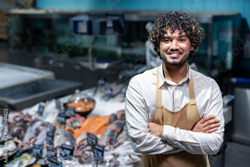 A smiling fishmonger stands confidently in front of a display of fresh seafood, ready to assist customers. He wears an apron.