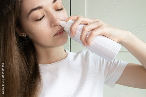 Fotografija Young woman rinsing her nose with saline solution spray bottle to relieve congestion, seasonal allergies, runny nose