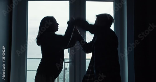 Silhouettes of a girl and a guy quarreling and holding each others hands in a gray house