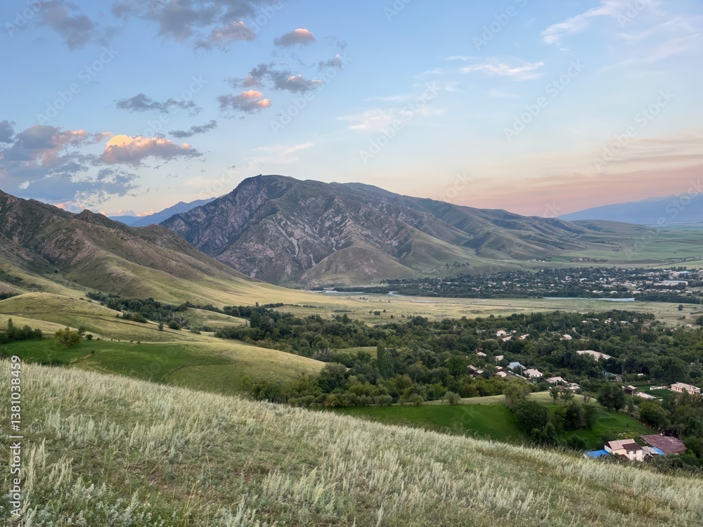Fototapeta premium rolling green hills and rugged mountains at sunset with a rural village and river in a picturesque valley, ideal for travel