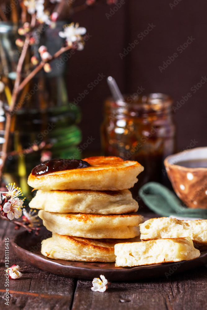 Lenten yeast pancakes with plum jam and tea, and a bouquet of blooming apricot branches on a wooden table.