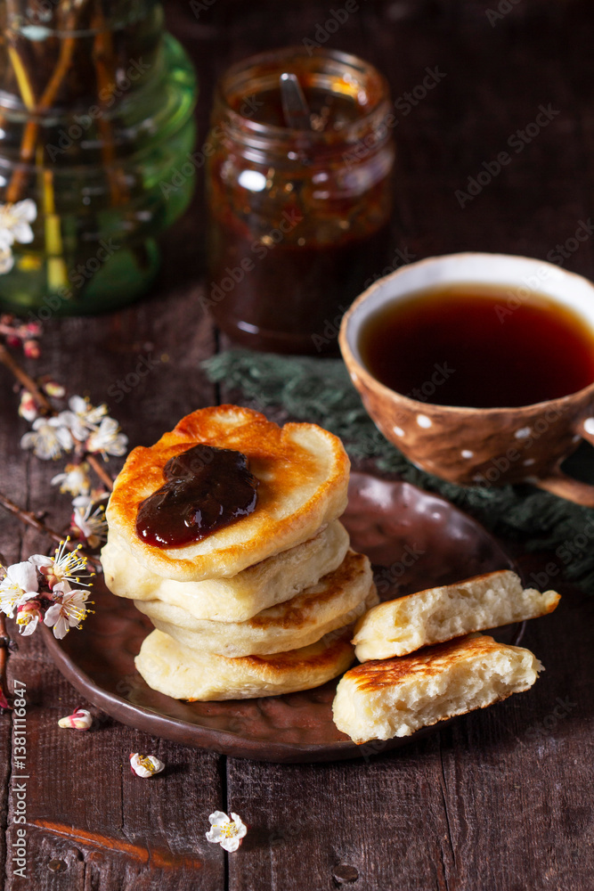 Lenten yeast pancakes with plum jam and tea, and a bouquet of blooming apricot branches on a wooden table.