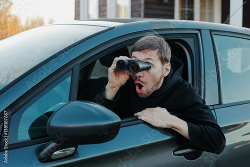 Fotografie Young shocked man stalker watching through binoculars sitting in car