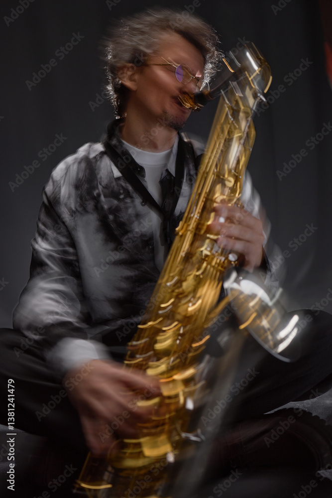Naklejka premium Vertical dynamic shot of male musician expressively playing saxophone sitting in grey studio with backlight, slow shutter effect