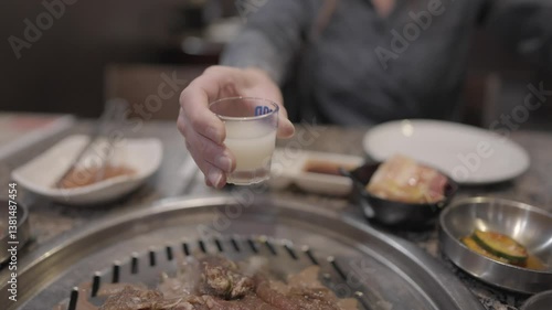 This video shows hands pouring soju from the bottle into a shot glass at a Korean bbq restaurant. 