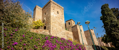 Exterior view of Alcazaba castle palace and moorish stronghold rising above street level and greenery against a vibrant blue sky
