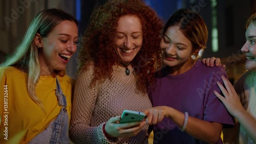 Multiracial happy smiling girl friends watching funny and surprising phone and smiling together outdoor at city night. Only women group technology addicted and social media. Fun youth communication