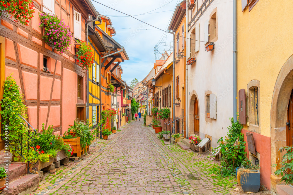 Fototapeta premium Colorful half-timbered buildings in a narrow cobblestone alley in the historic old town district of the touristic village of Eguisheim, France, in the Alsace region.
