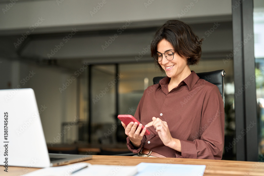 Happy female worker making payments on smartphone at work. Busy professional young business woman using mobile phone working in office. Smiling executive holding cell at desk. Happy female worker making payments on smartphone at work. Busy professional young business woman using mobile phone working in office. Smiling executive holding cell at desk.
