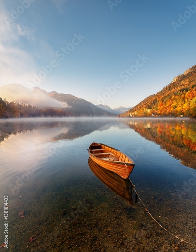 A small boat floating on a crystal-clear lake, surrounded by mountains under a soft morning mist