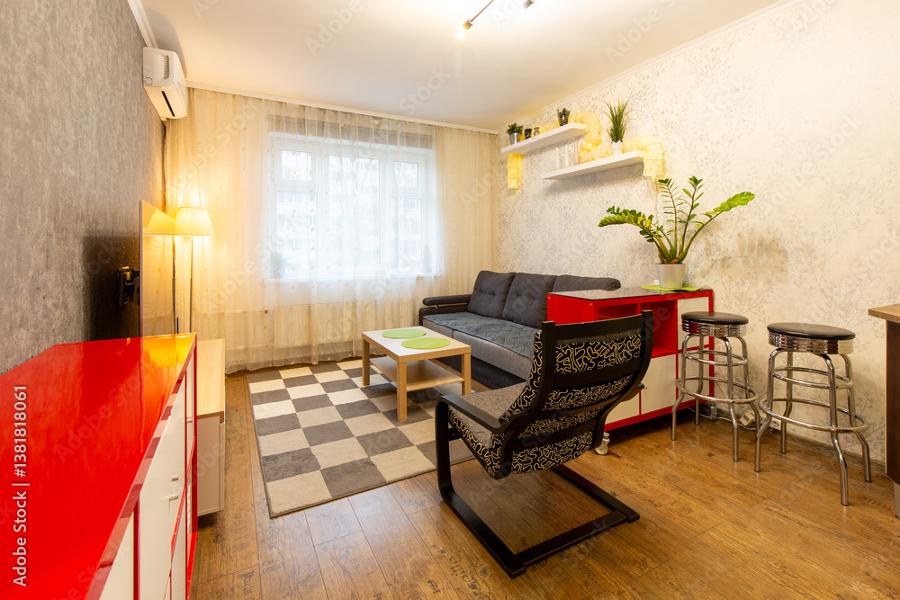 Apartment interior. Living room with furniture: armchair, sofa, red chest of drawers, metal chairs, wooden coffee table, shelves with indoor plants, TV. The window is covered with a tulle curtain.