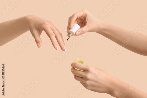 Female hands with bottle of cuticle oil on beige background