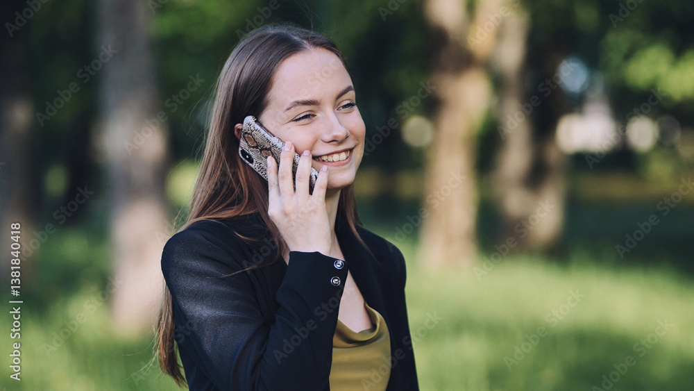 Professional woman talking on smartphone near trees, basking in warm sunlight Professional woman talking on smartphone near trees, basking in warm sunlight