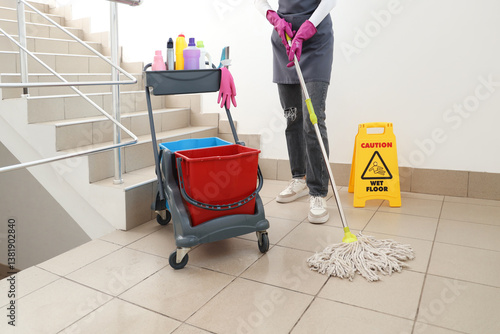 Konstfotografi Female janitor with trolley of cleaning supplies mopping floor in stairway