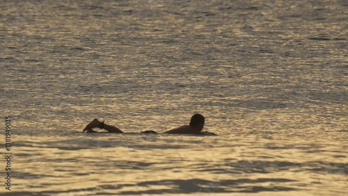 Adult male surfer swimming the Indian Ocean and waiting a wave at sunset time. Maldives. Slow motion video