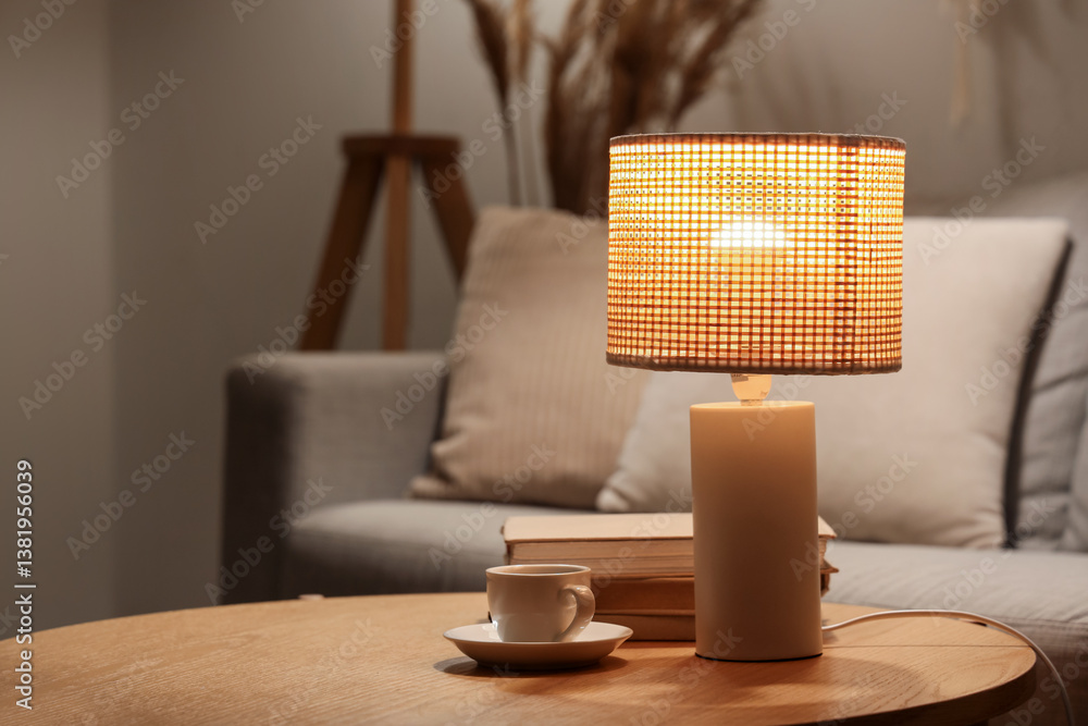 Glowing lamp with books and cup of coffee on table in living room at night