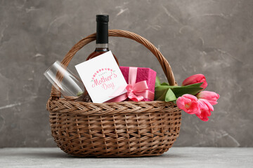 Basket with wine bottle, tulips and gift box for Mother's Day on table against grey grunge background