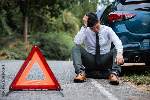 Bilde på lerret In the face of car trouble, a young businessman calmly changes the wheel of a broken car, while a worried mature man sits beside him