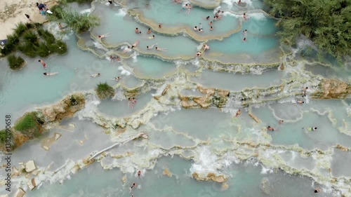 Aerial summer top-down view of Terme di Saturnia, geothermal sulfur springs and natural spa with waterfalls at Saturnia thermal baths. People bathing at Cascate del Mulino, Grosseto, Tuscany, Italy.