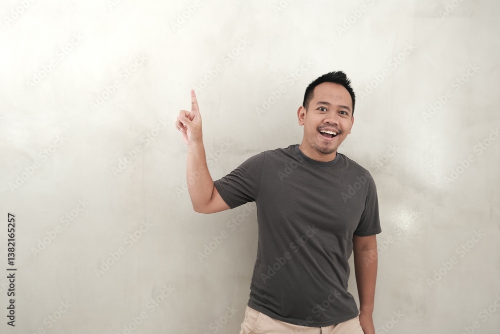 A young Indonesian man in casual grey t-shirt points to the left with copy space A young Indonesian man in casual grey t-shirt points to the left with copy space