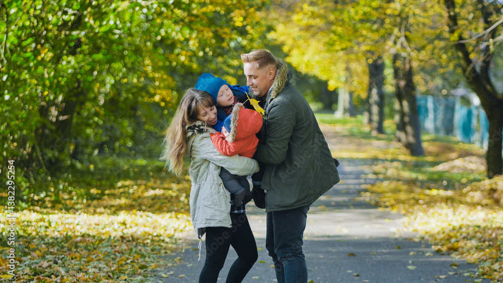 Obraz premium Parents playing with their two children in a park full of fallen leaves during a sunny autumn day