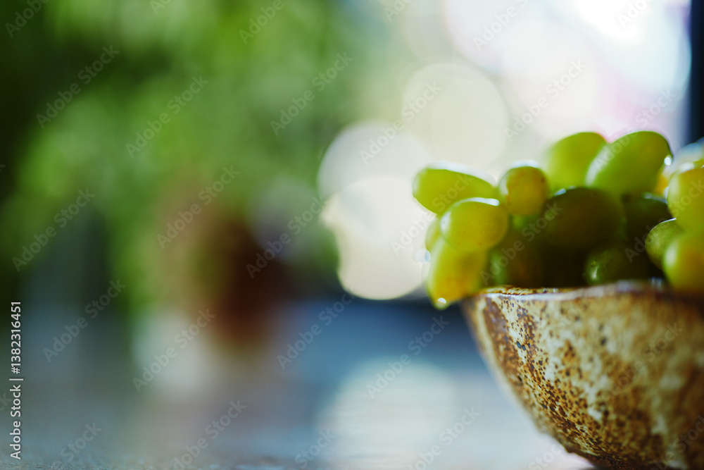 Fototapeta premium Closeup of ripe grapes in a bowl on a table in front of a window with natural light coming through