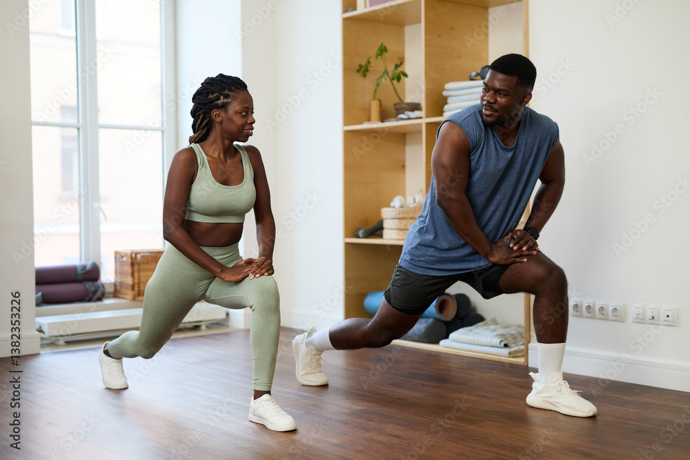 Obraz premium African American couple stretching legs while exercising in well-lit home gym