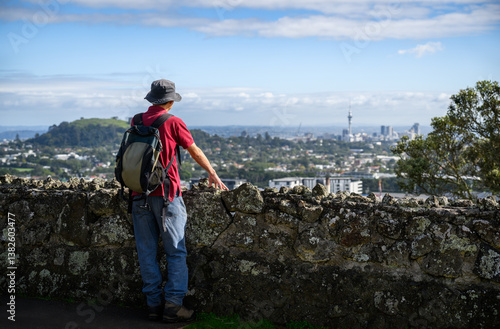 Man standing by stone wall on One Tree Hill, enjoying the views of Sky Tower and Auckland city.
