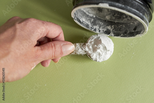 Close-up of a woman's hand, holding a measuring spoon of creatine. Creatine is a sports supplement.