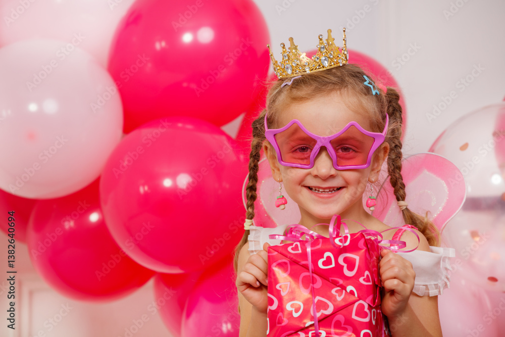 Joyful girl in a crown and star glasses, amidst pink balloons